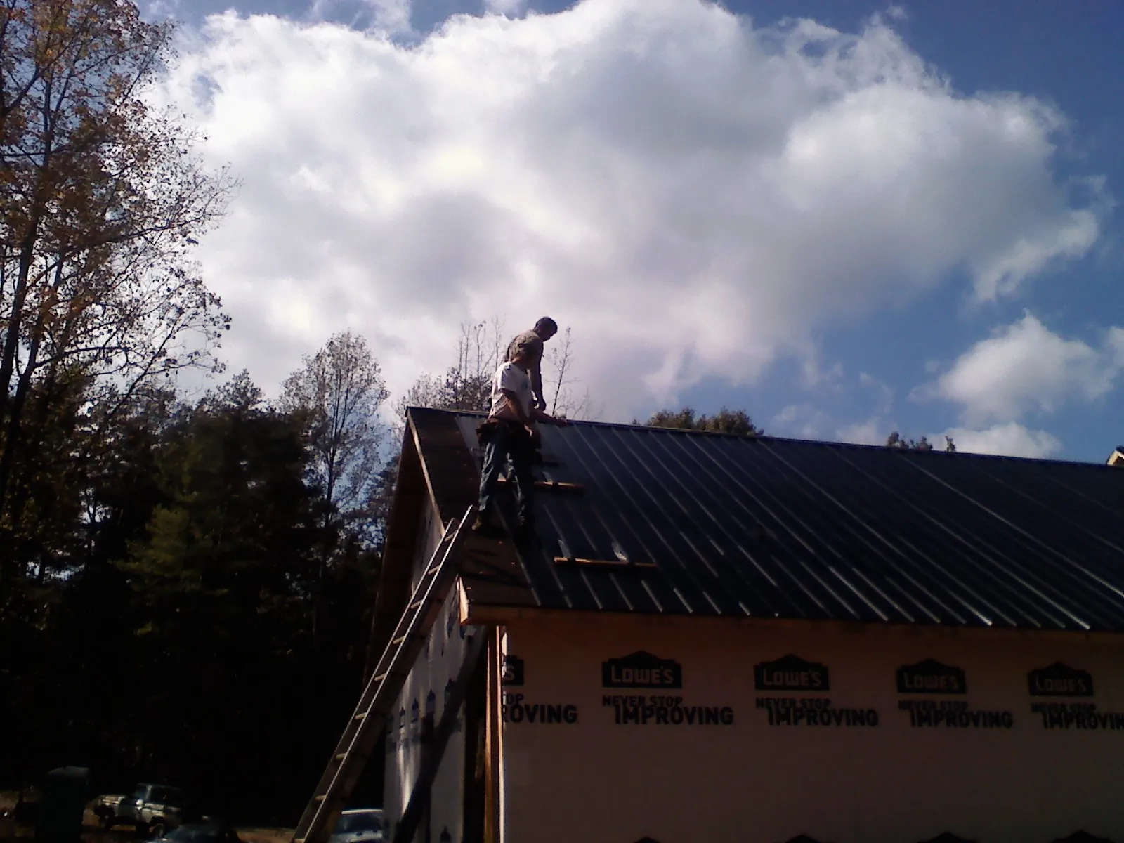 Roofer fastening dark metal panels high against a cloudy sky, from a Roof Inspection job in Terra Ceia