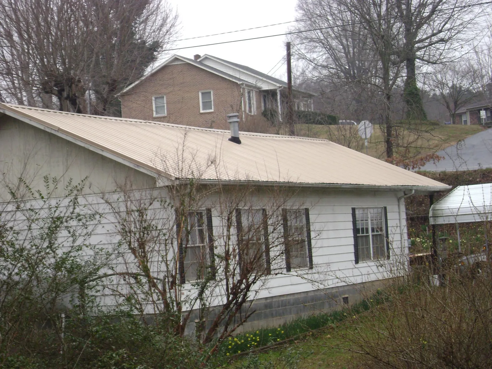 Tan metal roof on a white sided house set into a hillside — Commercial Roofing by Roofing Brothers in Terra Ceia